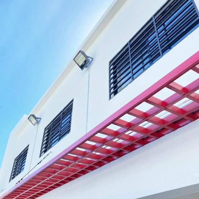 Fachada blanca con pérgola roja y celosías metálicas en proyecto de Don Bosco