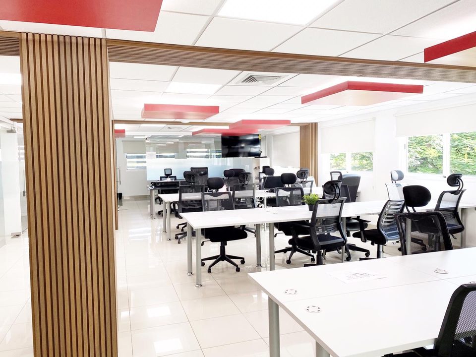 Oficina corporativa remodelada con escritorios blancos, plafones rojos y división de listones de madera en Santo Domingo